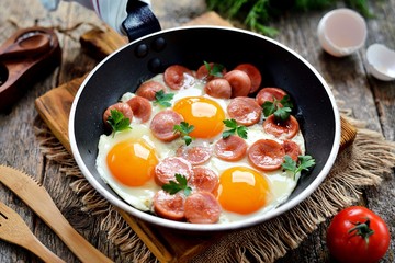 Homemade fried eggs with sausages in a frying pan on wooden background. Classic breakfast. Top view.