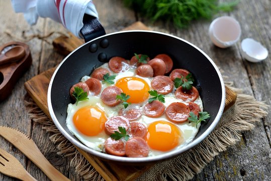 Homemade fried eggs with sausages in a frying pan on wooden background. Classic breakfast. Top view.