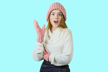 Beautiful girl in gloves with a sweater and winter hat raises her hand in surprise