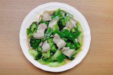 Stir Fried Broccoli, Peas with Crispy Pork with oyster sauce, Fried vegetable broccoli for food menu diet healthy in a dish on a wooden floor (Thai Foods)