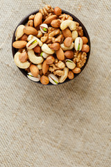 Mix of different nuts in a wooden cup against the background of fabric from burlap. Nuts as structure and background, macro. Top view.