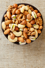 Mix of different nuts in a wooden cup against the background of fabric from burlap. Nuts as structure and background, macro. Top view.
