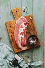 Raw beef bone meat on a cutting board, rustic green wooden table, spices, knife, hatchet. Top view, flat lay.
