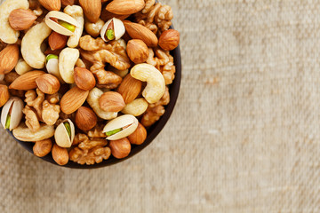 Mix of different nuts in a wooden cup against the background of fabric from burlap. Nuts as structure and background, macro. Top view.