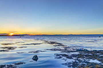 Fototapeta na wymiar Sunset in Rimouski, Quebec by Saint Lawrence river in Gaspesie region of Canada with dark floating seaweed