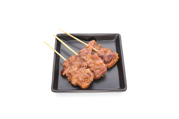 Pork barbecue sticks served on black square plate on isolated white background.