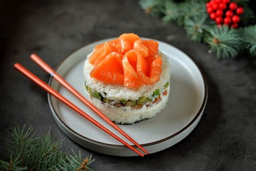 Homemade sushi cake with lightly salted salmon, avocado, soft cheese and seaweed. Christmas background.