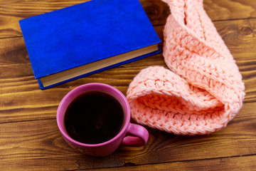 Cup of coffee, knitted scarf and book on wooden background