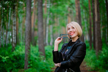 blonde girl holding glasses with a smile on her face in the forest