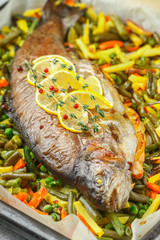 Baked fish trout with vegetables (potatoes, carrots, string beans, green peas and onions) with lemon, thyme and pink pepper. Wild salmon. Delicious healthy dinner.  Selective focus