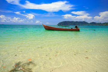 Fototapeta na wymiar A fishing boat floating on beach with clean and clear sea and cloudy blue sky. Copy space. 