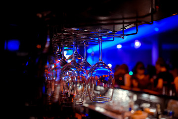 Clean glassware on the counter of a nightclub ready to serve customers, dimly lit with colorful...