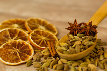 Pile of aromatic cardamom and spicy star anise in wooden spoon arranged on table with sweet dried oranges for Christmas Day