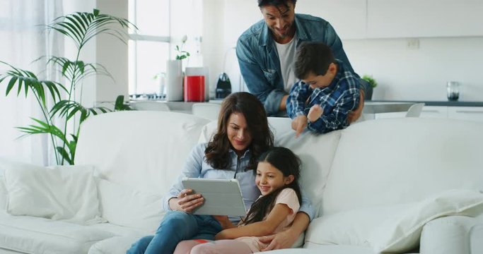 Portrait of happy family having fun using tablet on sofa in living room in slow motion. 