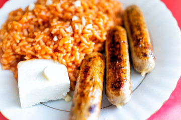 Closeup of large lunch dinner plate with fried three sausages, tomato red rice, cheese cube, orange color greasy unhealthy food