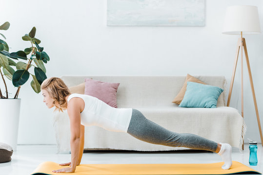 Attractive Woman Doing Push Ups On Yellow Fitness Mat Near Couch At Home