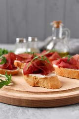 Canape or crostini with toasted baguette, light cheese, bresaola and arugula on wooden board. Diet food. Iron food.