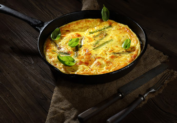 omelet with asparagus in a pan on a wooden background. rustic style.