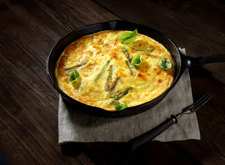 omelet with asparagus in a pan on a wooden background. rustic style.