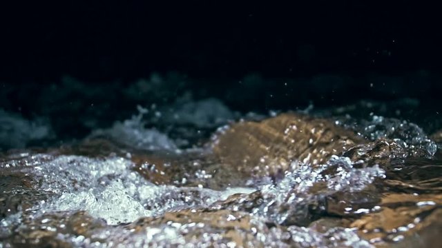 Slow motion of waves on dark water surface with play of flecks of bright light close up. Amazing dramatic natural background. Shooting with 180fps. Epic mystical and magic night view. Crystal clear