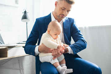 cute baby touching watch of handsome father in suit