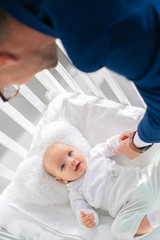 overhead view of father in suit holding hand of infant daughter in baby crib