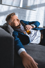 Fototapeta na wymiar drunk businessman lying on sofa and drinking alcohol from bottle