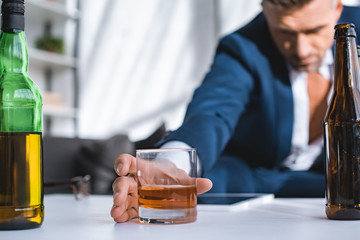 selective focus of glass with whiskey in hand of drunk businessman