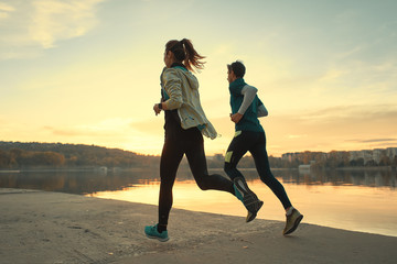 Young man and woman out for a run on the lake at the sunrise