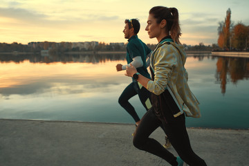 Young man and woman out for a run on the lake at the sunrise