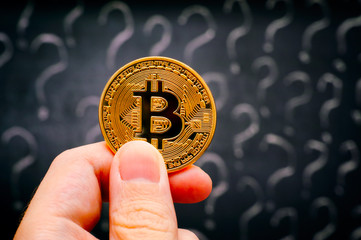 Person hand with Bitcoin virtual money against blackboard with question marks.