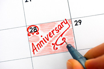 Woman fingers with pen writing reminder Anniversary in calendar.