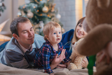 Happy family with a child spend Christmas together. Parents and daughter play at home near the Christmas tree. - Image