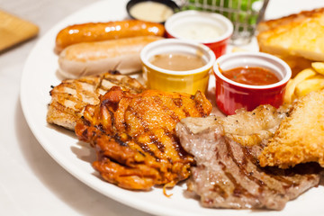 Food Steaks and Sausages Assortment (Spicy Chicken, Pork, Beef, Fish) served with French Fried and baked bread, sided with varieties of sauces and farm fresh vegetable in white dish table background.