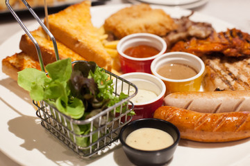 Food Steaks and Sausages Assortment (Spicy Chicken, Pork, Beef, Fish) served with French Fried and baked bread, sided with varieties of sauces and farm fresh vegetable in white dish table background.