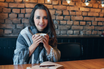 Portrait of young lady with dark curly hair dreamily closing her eyes with cup in hands. Nice girl sitting in cafe with cup of coffee