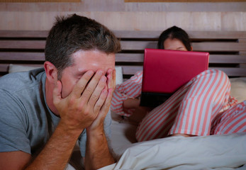 Obraz premium angry and frustrated husband moody in bed ignored by his workaholic wife or internet social media addict girlfriend using laptop in bed ignoring the man in couple problem