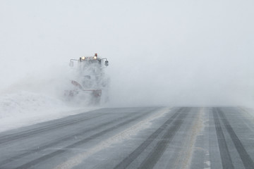 Snowblower grader clears snow covered  road. A  heavy snowstorm swept the road. Car in the snow.