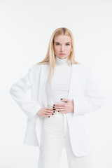 attractive caucasian blonde woman in fashionable white clothes touching stomach and looking at camera isolated on white