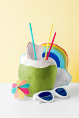 Fresh coconut on a pastel yellow background with rainbow cloud inflatable drink holder and...