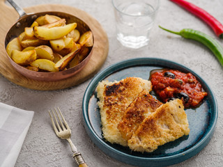 Fried fish with tomato-olive sauce and potatoes.