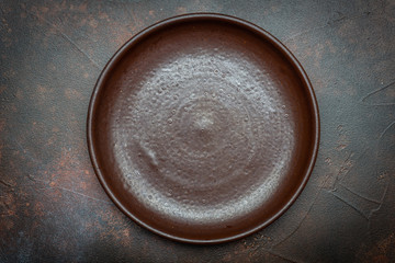 Empty brown plate (ceramic) on a dark background with a knife and fork. Copy space.