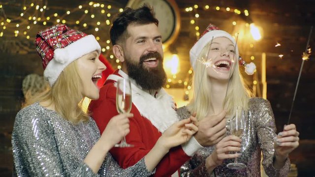 Bearded man in santas costume and two girls in New Year's hats burn Bengal lights and have fun celebrating Christmas. Happy New Year and Christmas. New Year's mood. New Years party.