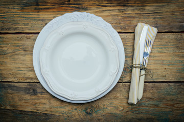 Empty white rustic plate on old wooden background with knife, fork and napkin. Rustic food concept. Copy space