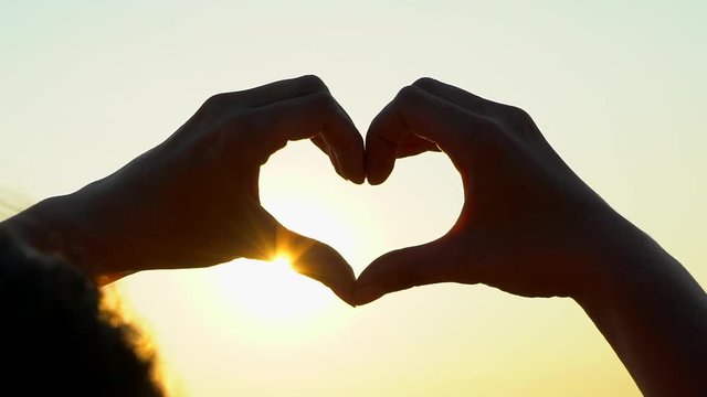 sunset heart hands. Woman shapes heart with hands over sun on sunrise or sunset in nature summer. Male making heart shape against sun, Girl holding up love symbol gesture sun background, freedom dream