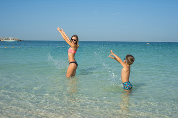 Happy smiling mother and her son playing and running on the beach. Concept of friendly family - Image. Happy summer days is coming