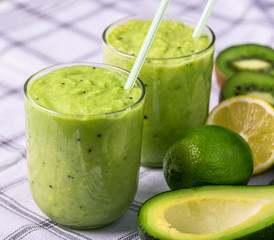 Green smoothie on tablecloth with avocado, lemon and kiwi on the right side.