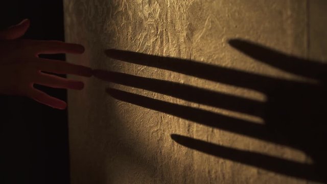 Shadow play. Black shadow of arm and fingers plays on the wall in orange light