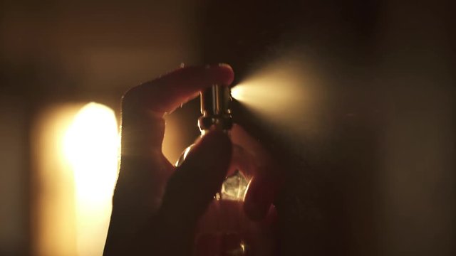 Young woman squirting perfume on her neck in a room with orange sunset light