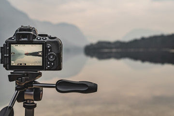 Camera on tripod at work on a misty lakeshore. Camera display. Taking pictures using the display.